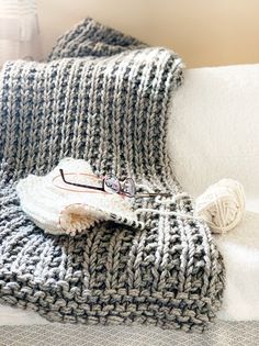 a knitted blanket and ball of yarn sitting on top of a white couch cushion