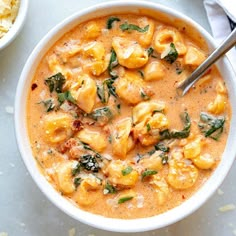 a white bowl filled with pasta and spinach on top of a table next to other dishes