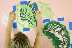 a woman is painting on the wall with palm leaves