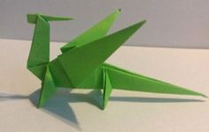 a green origami bird sitting on top of a white table next to a wall