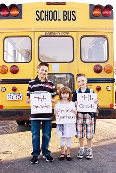 three children holding up signs in front of a school bus