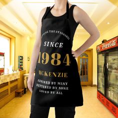 a woman standing in front of a vending machine wearing an apron that says since 1994