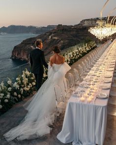 a bride and groom standing next to each other at a long table with candles on it