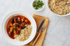 a white bowl filled with meat and rice next to a fork, spoon and napkin