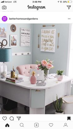 a white desk topped with lots of pink flowers next to a lamp and pictures on the wall