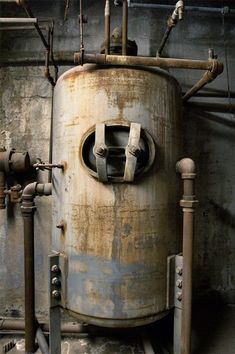 an old, rusty tank sits in the middle of a room with pipes and piping