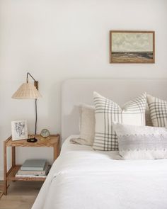 a bed with white linens and pillows in a small room next to a painting on the wall