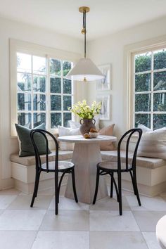 a table with two chairs and a vase on it in front of three large windows