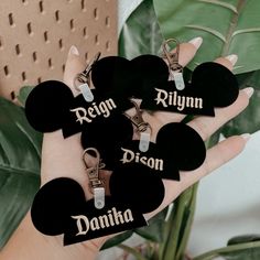 a hand holding four black heart shaped key chains with name tags attached to each one