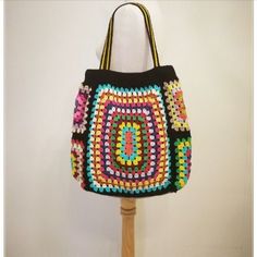 a multicolored crocheted bag sitting on top of a wooden stand next to a white wall