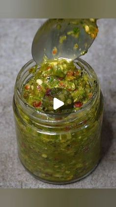 a glass jar filled with green sauce on top of a counter next to a spoon