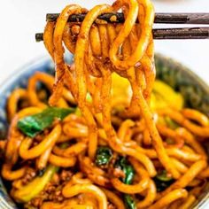 noodles being lifted from a bowl with chopsticks over them and sauce on the side