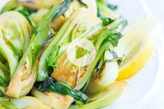 a white plate topped with green vegetables and lemon wedges