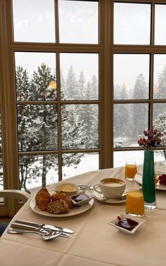 a table with breakfast food and drinks on it in front of a window overlooking the snow covered mountains