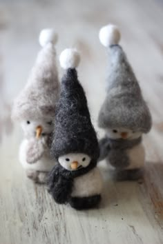 three small stuffed penguins sitting next to each other on top of a wooden table with white and gray decorations