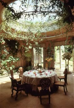 a dining room with a round table surrounded by greenery