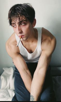 a young man sitting on top of a bed with his hand under his chin and looking at the camera