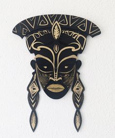 a black mask hanging on the wall next to a white wall with geometric designs and gold accents