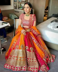 a woman sitting on top of a bed wearing an orange and pink lehenga