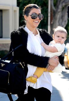 a woman holding a baby in her arms while walking down the street with another person