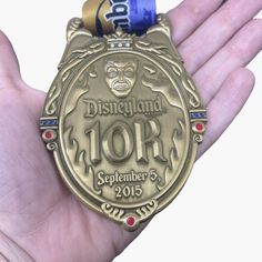 a hand holding a gold medal with a blue ribbon around it's neck and the words disneyland 101rd on it