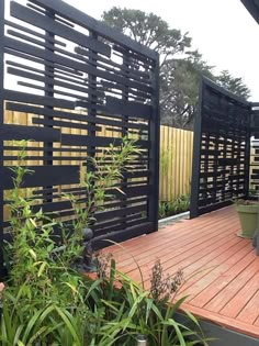 a wooden deck surrounded by plants next to a fenced in area with potted plants