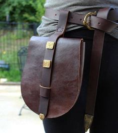 a person wearing black pants and holding a brown leather bag with gold hardwares on it