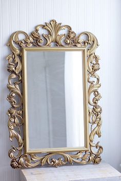 an ornate gold framed mirror sitting on top of a white table next to a wall