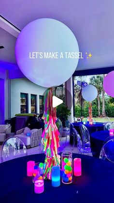 a table with balloons and candles on it in front of a large window that says let's make a tassel