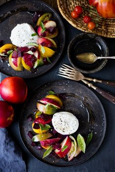 two black plates with food on them next to some apples and other fruit in bowls