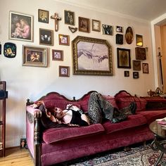 a woman laying on top of a red couch next to a wall covered in pictures