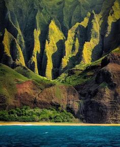 the mountains are covered with green vegetation and blue water in front of an ocean shore