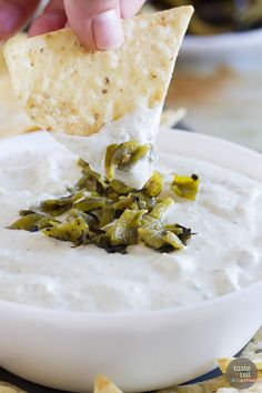 a hand dipping a tortilla chip into a bowl of white dip