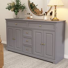 a white dresser topped with a mirror next to a lamp and pictures on the wall