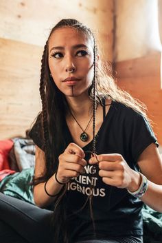 a woman with long braids sitting on a bed looking at the camera and making a funny face