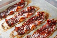 bacon strips are lined up on a baking sheet