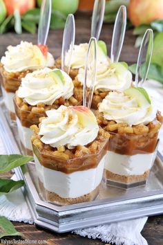 mini desserts with apples and whipped cream on a silver tray next to green leaves