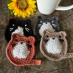 three crocheted cat coasters sitting next to a coffee cup and sunflower