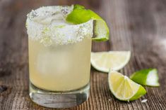 a close up of a drink on a table with limes and salt in the background