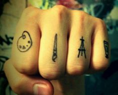 two fingers with small tattoos on them, one has an eiffel tower and the other has scissors