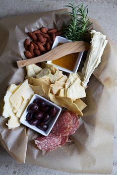 an assortment of cheeses, crackers and olives on a paper wrapper