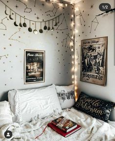 a white bed topped with pillows and blankets next to a wall covered in string lights