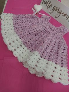 a crocheted baby dress is displayed on a pink tablecloth with a sign that says hello gorgeous