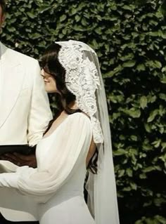 a bride and groom standing next to each other in front of a green wall with ivy