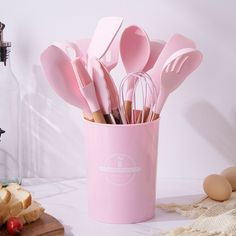 pink utensils and spoons are in a cup on a counter next to bread