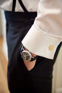 a man wearing a white shirt and black pants with a watch on his wrist in front of him