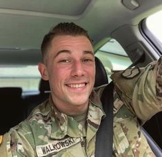 a man in uniform sitting in the back seat of a car with his hand up