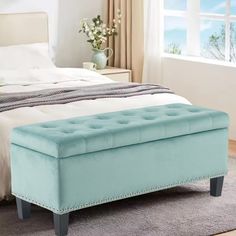 a blue bench sitting on top of a bed next to a white dresser and window