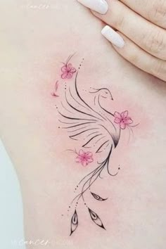 a woman's back with a bird and flowers tattoo on her left side ribcage