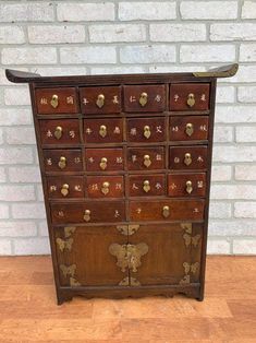 an old wooden chest with many drawers and brass knobs on the front, against a white brick wall